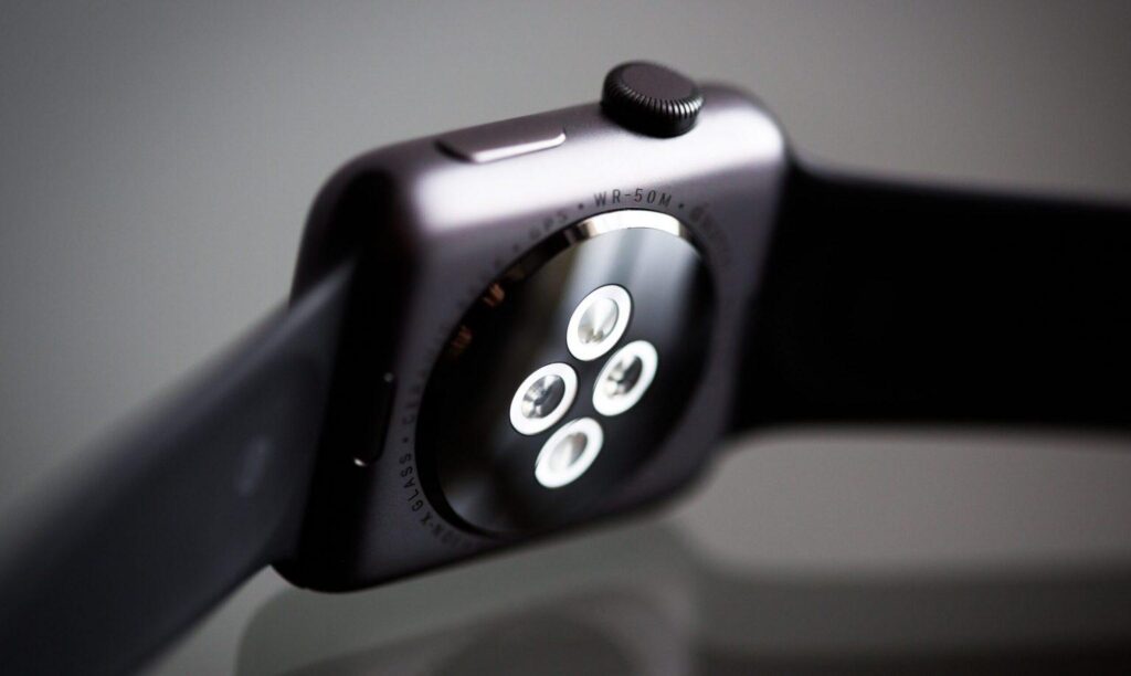Close-up of a smartwatch underside with four glowing sensors. The watch has a black band and matte finish.