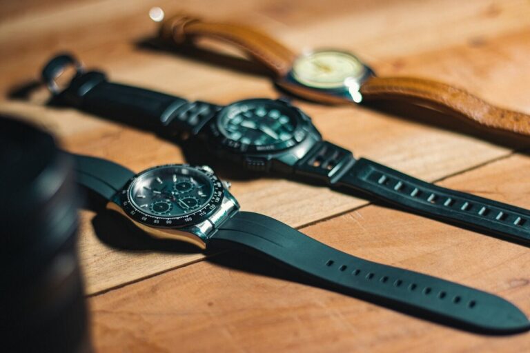 Three wristwatches with different watch materials: black rubber and steel, plastic, and brown leather with light dial on a wooden surface.