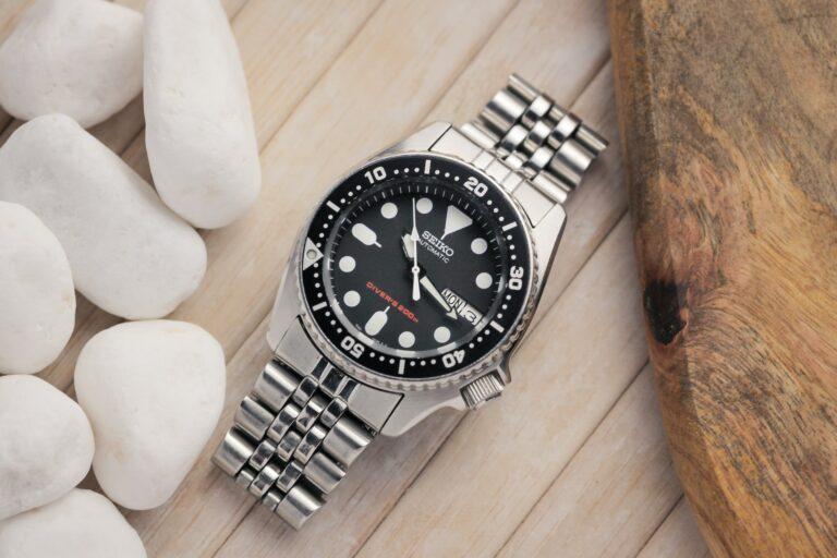 A black dial Seiko dive watch with a stainless steel bracelet sitting on a wooden table