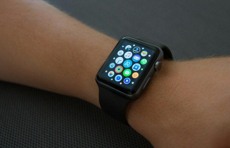 A smartwatch with a black band displaying colorful app icons on a person's wrist against a dark, textured background.