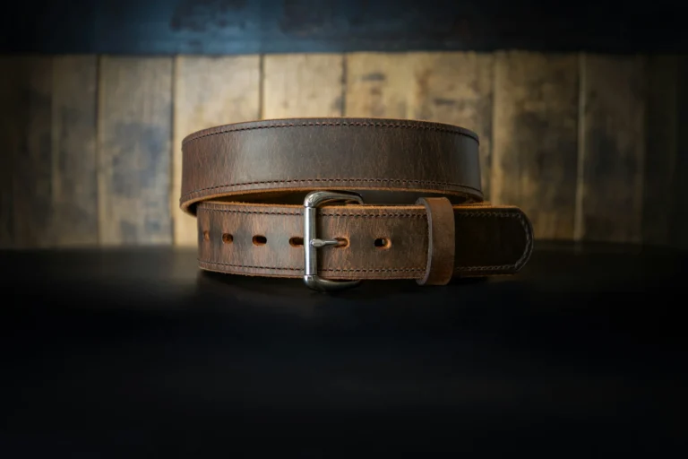 A brown leather belt with a silver buckle is coiled on a dark surface. The background features rustic wooden planks, giving a vintage feel.