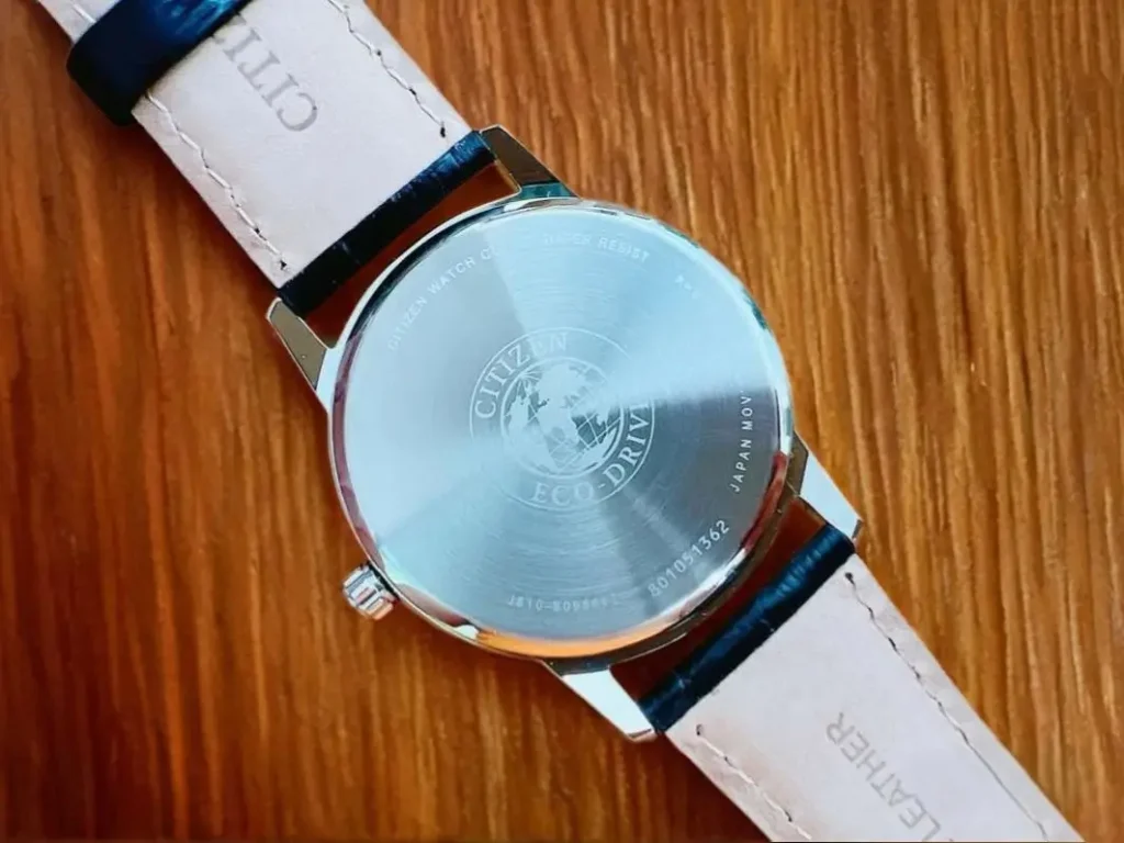 Close-up of the Citizen Corso Eco-Drive AW1236-03A watch case back, placed on a wooden surface.