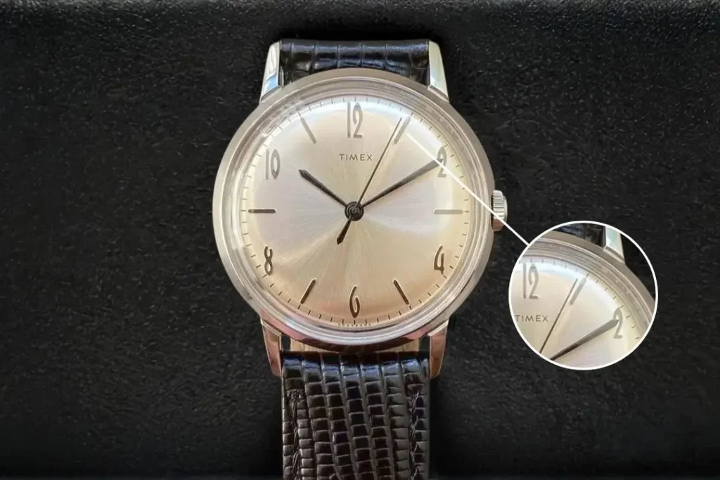 Timex Marlin Hand-Wound TW2R47900 on a black leather surface, with a magnified view showing the minute and seconds hands near the edge of the minute track.