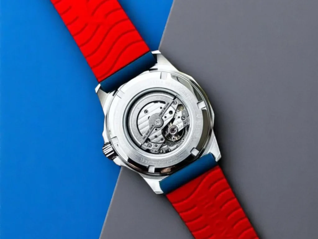 Bulova Marine Star 98A225 watch back with intricate movement details, featuring a vibrant red rubber strap on blue-gray background.