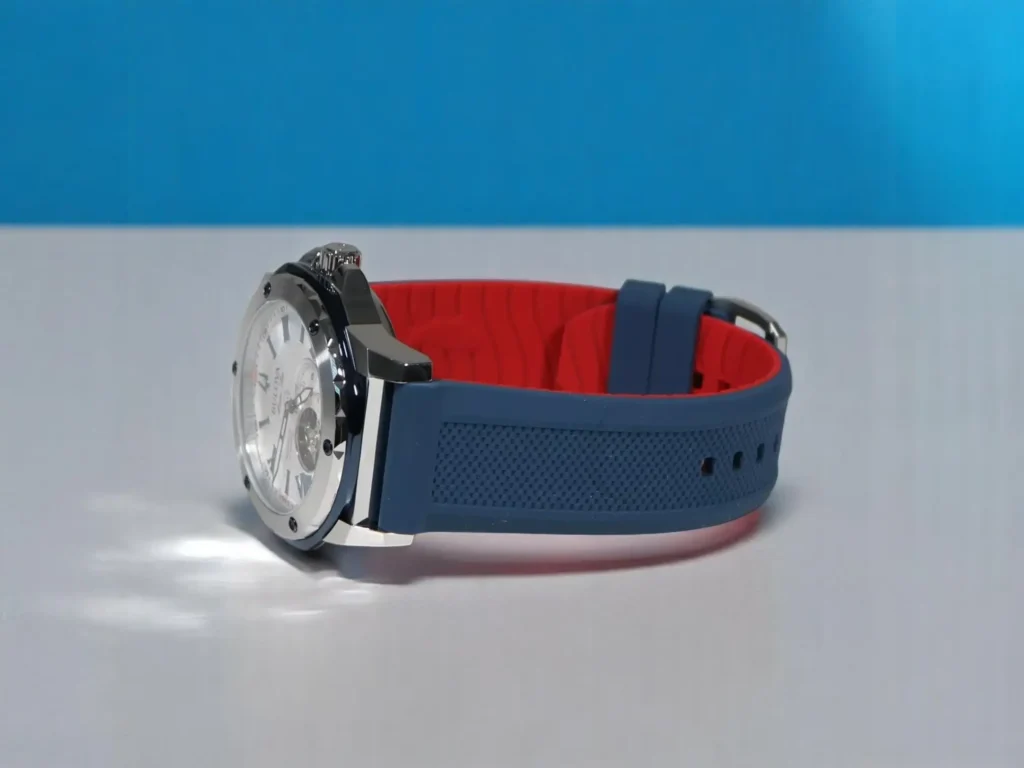 Bulova Marine Star 98A225 with a blue and red rubber strap, displayed on a gray surface against a vibrant blue backdrop.