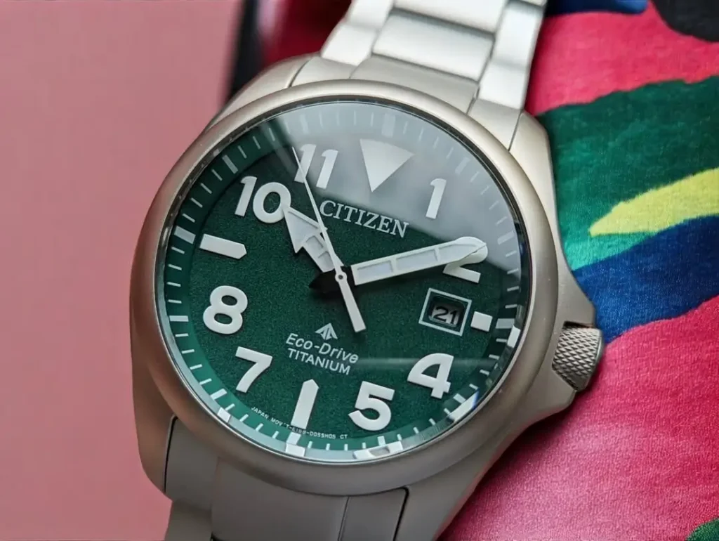 Close-up of Citizen Promaster Tough BN0241-59W green dial with luminous hands and markers, placed on a woven fabric.