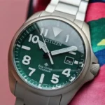 Close-up of Citizen Promaster Tough BN0241-59W green dial with luminous hands and markers, placed on a woven fabric.