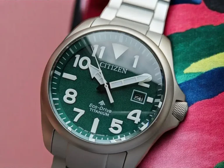 Close-up of Citizen Promaster Tough BN0241-59W green dial with luminous hands and markers, placed on a woven fabric.