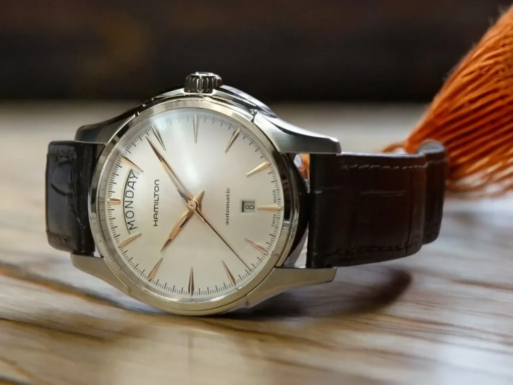 Hamilton Jazzmaster Day Date Auto dress watch displayed on a light tan wooden surface with classic and sophisticated design elements.
