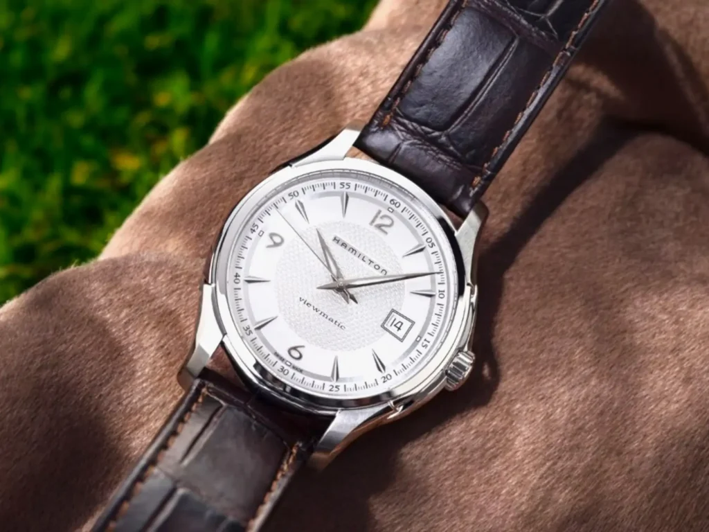 Hamilton Jazzmaster Viewmatic Auto dress watch centered on a plush surface with a blurred green outdoor background, highlighted by soft, natural lighting.
