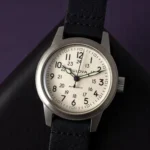 Close-up of the Bulova Hack Watch 96A246 resting on black textured leather with a dark purple wall in the background.
