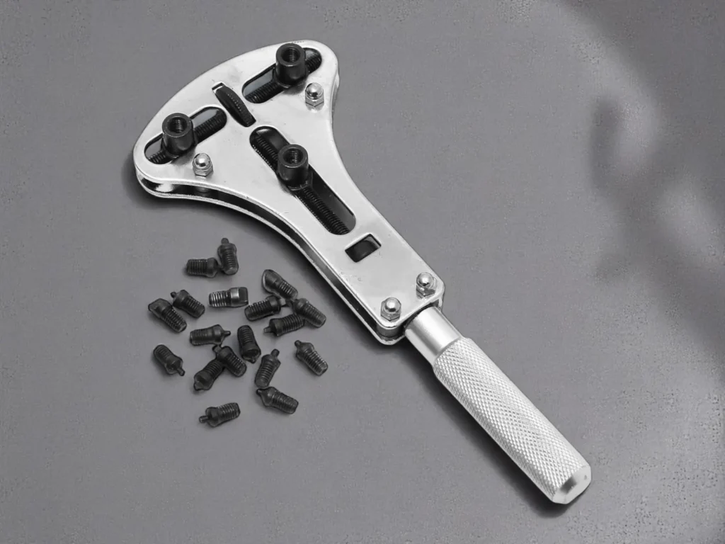 A silver Jaxa wrench for removing watch backs with a textured handle rests on a gray surface.