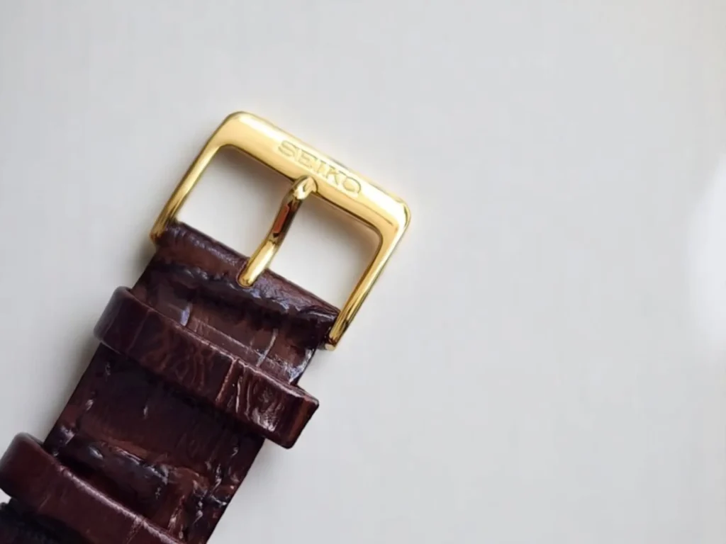 Close-up of a brown leather watch strap with a gold-tone buckle, engraved with "Seiko," on a plain white background.