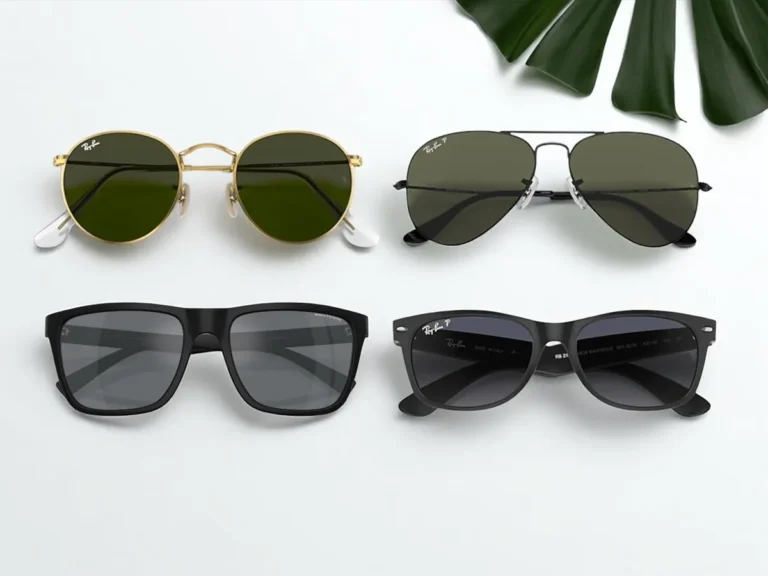 Four pairs of sunglasses on a white surface: round gold frames with green lenses, black aviators, rectangular frames, and classic wayfarers, alongside a green leaf.