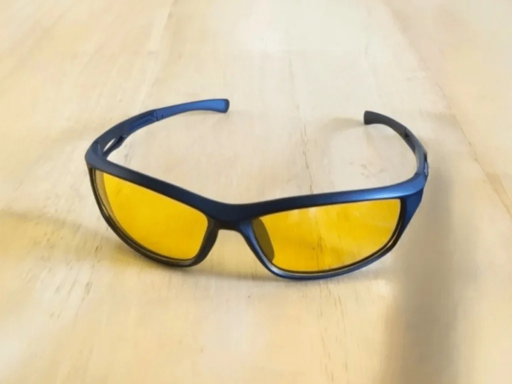 Duduma Polarized Sports sunglasses with a dark frame and yellow lenses rest on a light wooden surface.