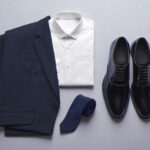 Navy suit jacket, white dress shirt, dark blue tie, and polished black shoes arranged on a light gray background, ideal for men's job interviews.