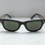Black Ray-Ban Wayfarer luxury sunglasses with dark lenses resting on a light gray marble surface.