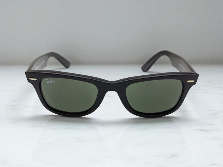 Black Ray-Ban Wayfarer luxury sunglasses with dark lenses resting on a light gray marble surface.