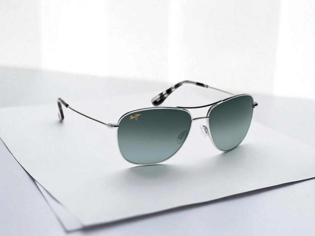 Sleek aviator sunglasses with titanium frame and blue-tinted lenses, placed on overlapping white sheets.