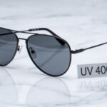 Black aviator sunglasses with dark lenses sit on a marble surface, next to a card that says "UV 400" for full UV protection.