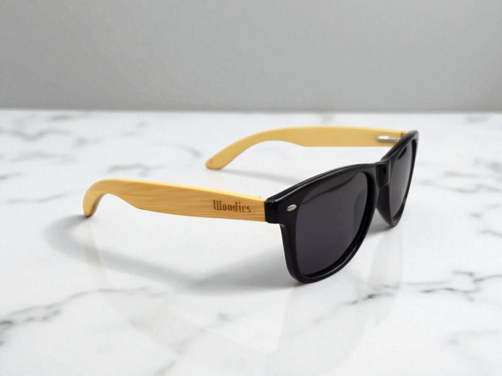 Sunglasses with black frames and light wooden arms on a white marble surface. 