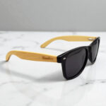 Sunglasses with black frames and light wooden arms on a white marble surface.