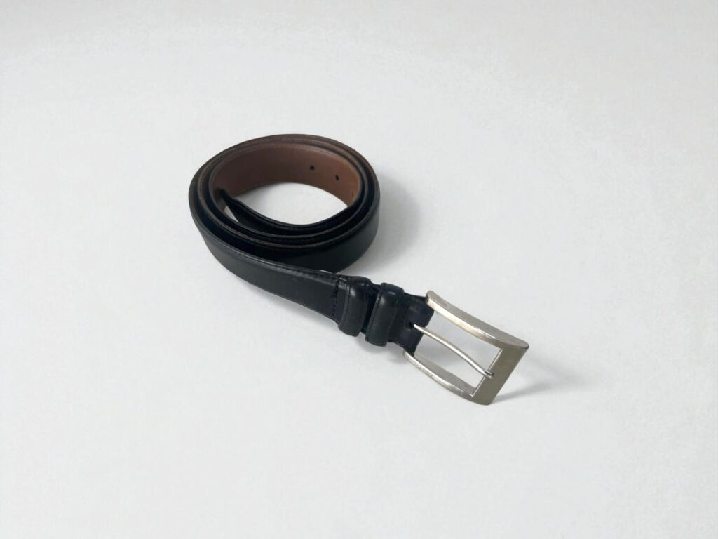 A coiled Allen Edmonds Wide Basic black leather belt with a silver buckle is placed on a clean, white surface.