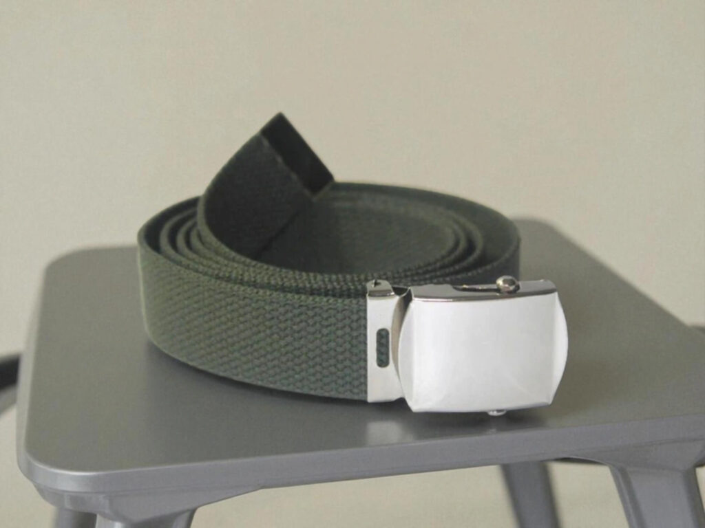 A dark green canvas belt with a shiny silver clasp is neatly coiled on a gray surface.