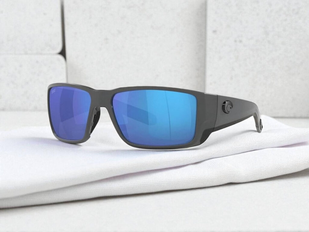 Costa Del Mar Blackfin polarized sunglasses with reflective blue lenses rest on a folded white cloth. 