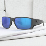 Costa Del Mar Blackfin polarized sunglasses with reflective blue lenses rest on a folded white cloth.