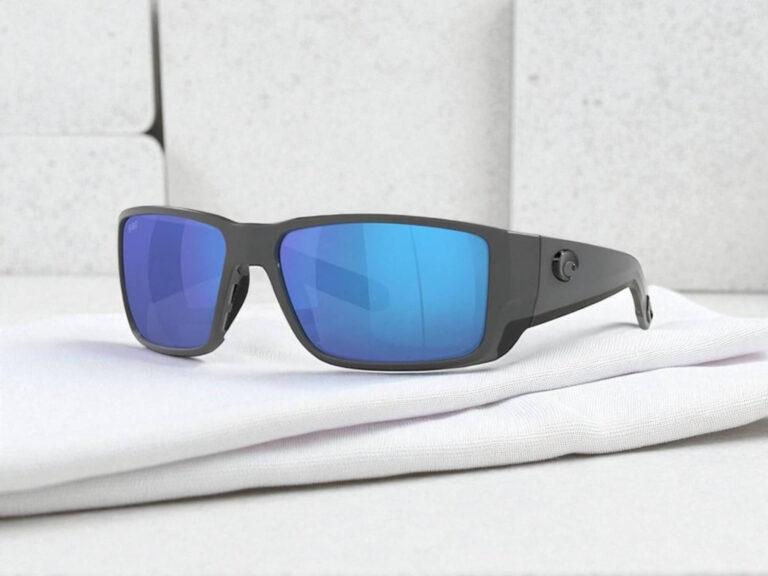 Costa Del Mar Blackfin polarized sunglasses with reflective blue lenses rest on a folded white cloth.