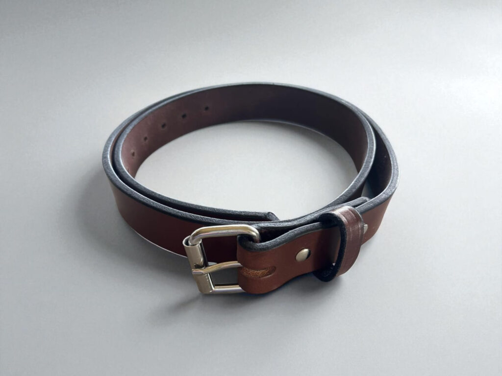 Brown Hank's The Gunner leather belt with a silver buckle, coiled on a light gray surface.