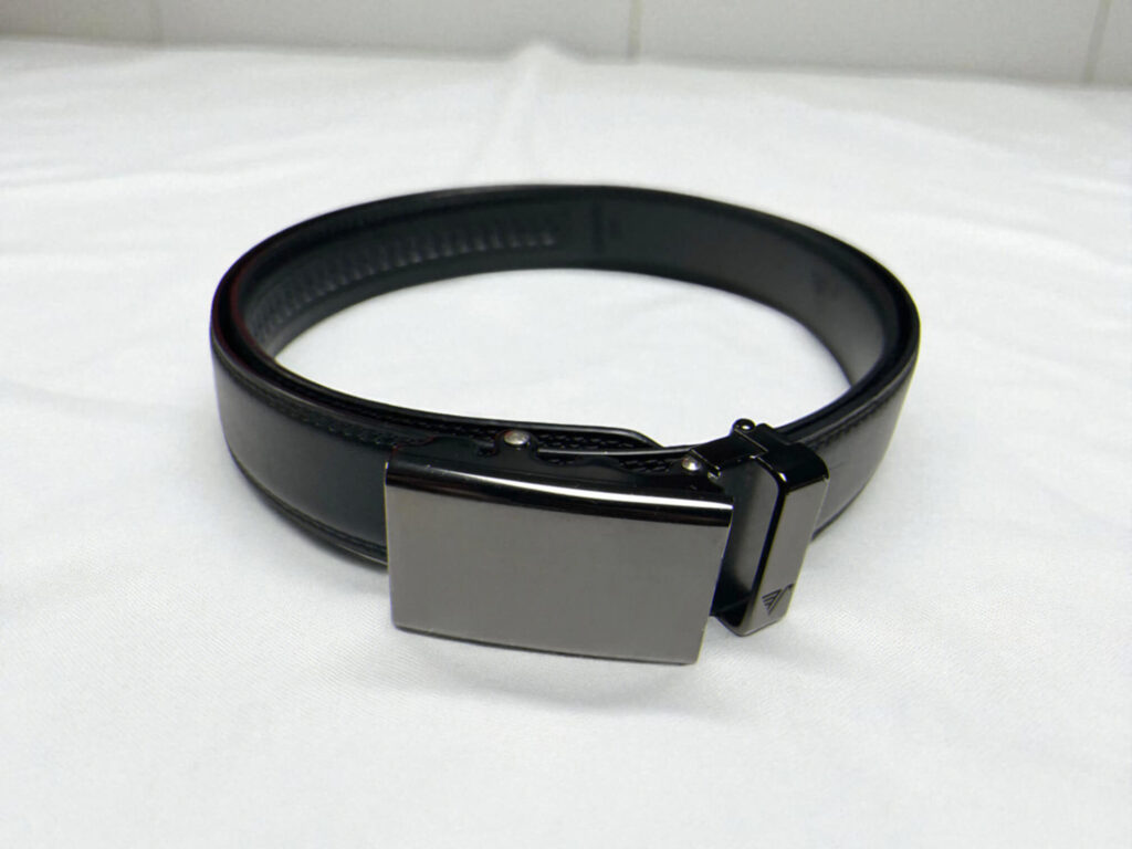 Mission Belt black leather dress belt with a smooth, rectangular metal buckle is coiled on a white surface.