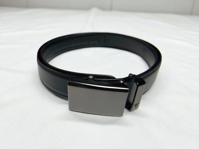 Mission Belt black leather dress belt with a smooth, rectangular metal buckle is coiled on a white surface.