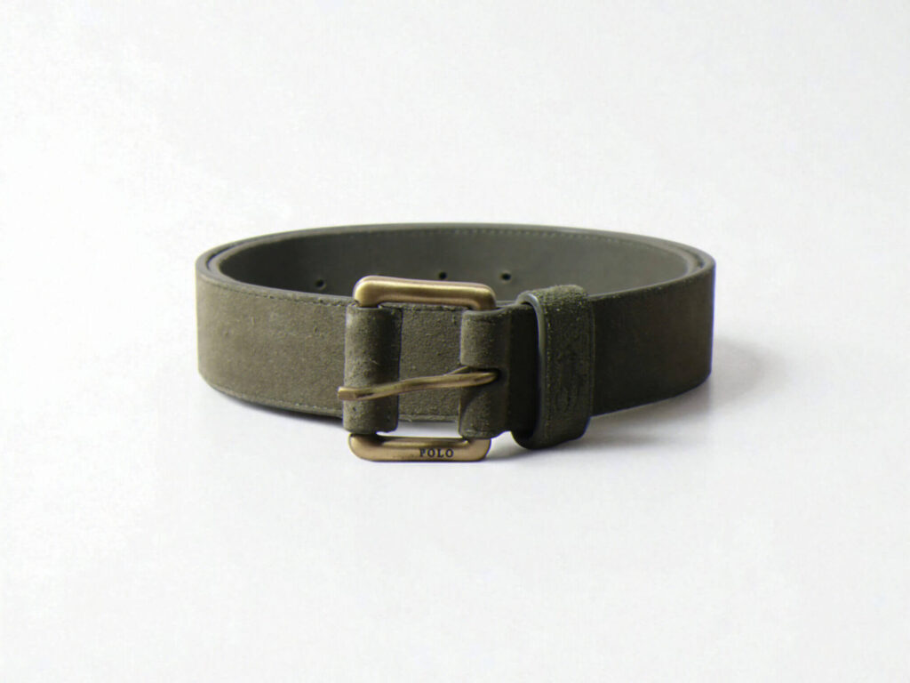 A dark olive suede belt with a bronze metal buckle, positioned in a loose circle on a plain white background.