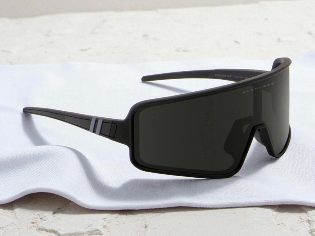 Blenders Eclipse Concord Fast running sunglasses with a wide, rectangular frame and dark lenses rest on a soft, white cloth.