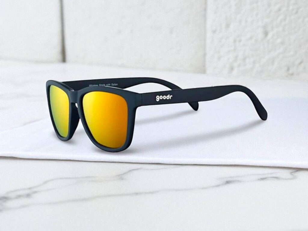 Goodr The OGs polarized sunglasses with vibrant orange reflective lenses, featuring the word "goodr" on the side, rest on a white surface with a marble background.