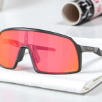 Oakley Sutro S running sunglasses with a black frame and large red lenses rest on a white cloth.