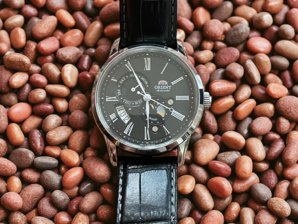 Orient RA-AK00 watch with a leather strap placed on a bed of variously colored stones.