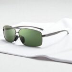 Sungait rectangular polarized sunglasses with green lenses and metallic frames rest on a smooth, white surface.