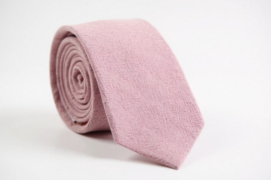 A neatly rolled DAZI pink cotton tie with a subtle texture is displayed against a plain white background.