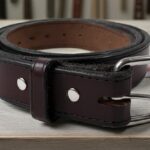 A coiled, dark brown Hanks leather belt with a silver buckle sits on a light wooden table.