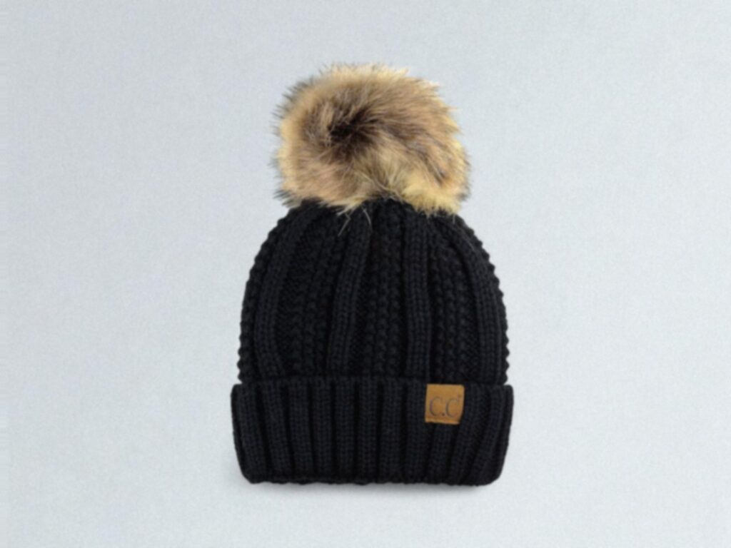 A black knit beanie with a large, fluffy faux fur pom-pom on top. 