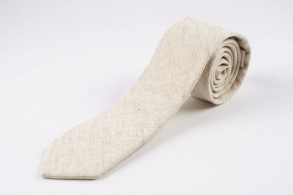 A beige cotton necktie rolled up neatly on a white background. The tie has a subtle textured pattern.