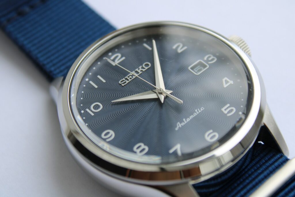 Close-up of a Seiko automatic watch with a polished case, dark blue textured dial, and a matching textured blue strap.