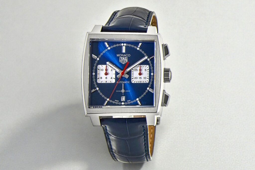 TAG Heuer Monaco Chronograph square-shaped watch featuring a blue face, silver indices, and red hands, with two square sub-dials and a blue leather strap.