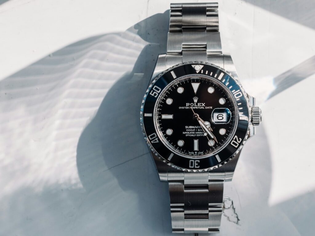 A stainless steel Rolex Submariner Date automatic watch with a black dial and bezel is shown lying on a white surface in natural light.
