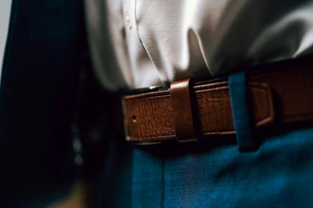 Close-up of a person wearing a white shirt tucked into blue trousers with a brown leather belt. 