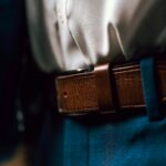 Close-up of a person wearing a white shirt tucked into blue trousers with a brown leather belt.