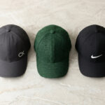 Three baseball caps made of cotton, wool, and polyester are displayed on a textured surface: a grey cap with a CK logo, a green cap in the center, and a black cap with a white swoosh logo.